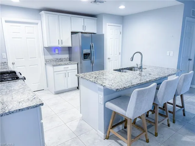 Kitchen featuring white cabinets, sink, stainless steel fridge, and light tile flooring