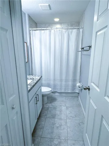 Bathroom with tile floors, a textured ceiling, vanity, and toilet