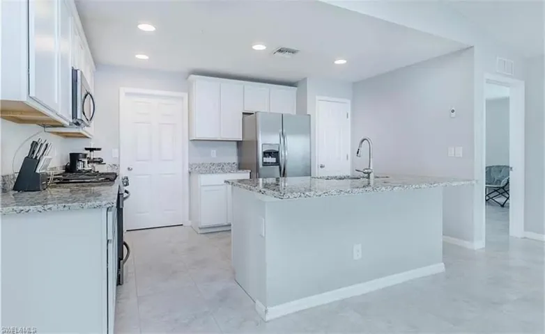 Kitchen with light tile flooring, a center island with sink, light stone countertops, white cabinets, and appliances with stainless steel finishes