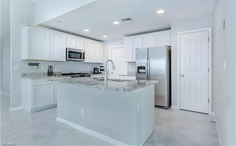 Kitchen with stainless steel appliances, white cabinets, sink, and light tile floors