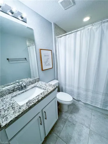 Bathroom with vanity with extensive cabinet space, a textured ceiling, toilet, and tile floors