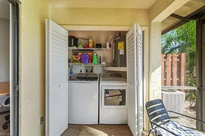Washroom featuring a textured wall, electric water heater, and washer and clothes dryer