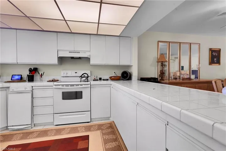 Kitchen featuring tile countertops, electric stove, white cabinets, and under cabinet range hood