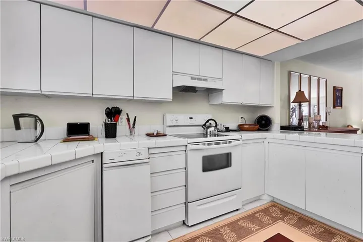 Kitchen with tile counters, white electric range, white cabinetry, and under cabinet range hood