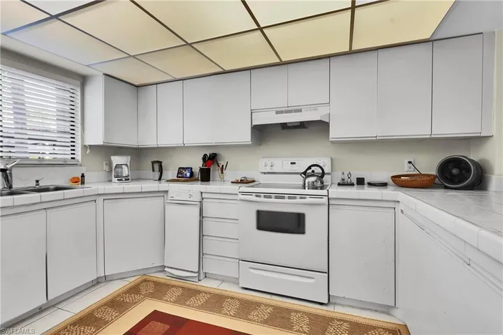 Kitchen featuring tile countertops, white range with electric cooktop, light tile patterned flooring, white cabinetry, and under cabinet range hood