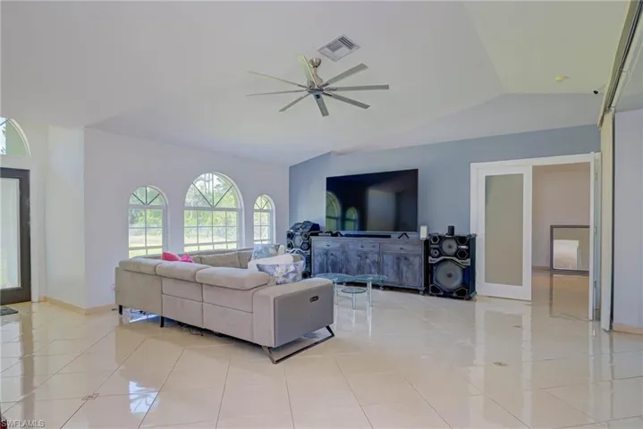 Living area with vaulted ceiling, a ceiling fan, and light tile patterned floors