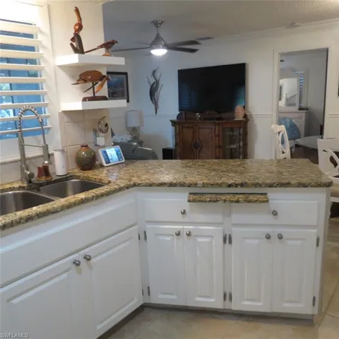 Kitchen featuring ceiling fan, crown molding, sink, white cabinets, and light tile patterned floors