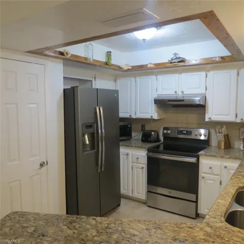 Kitchen featuring white cabinets, appliances with stainless steel finishes, light stone countertops, and decorative backsplash