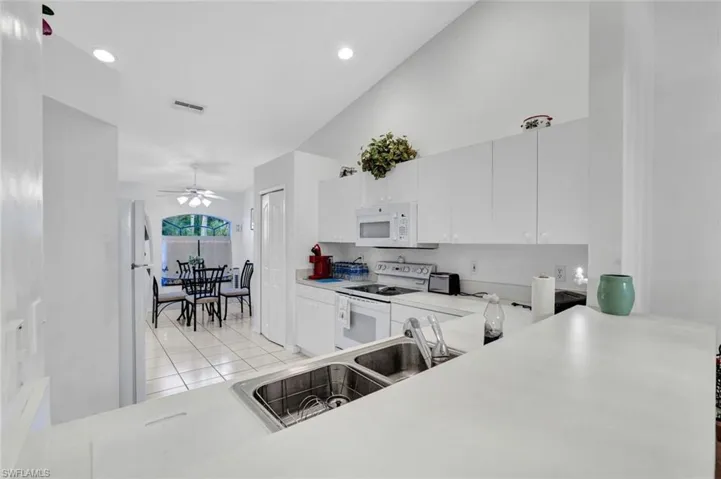 Kitchen with white appliances, light tile patterned flooring, white cabinetry, ceiling fan, and vaulted ceiling