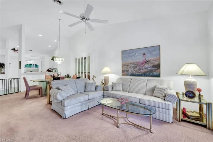 Living room featuring light carpet, ceiling fan with notable chandelier, and vaulted ceiling