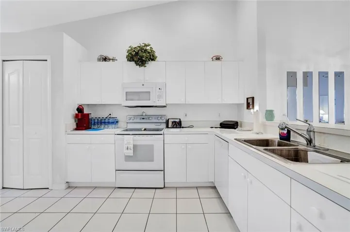 Kitchen featuring lofted ceiling, white cabinetry, light tile patterned flooring, sink, and white appliances