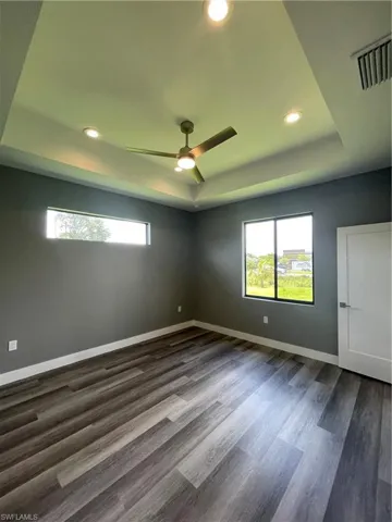 Empty room with a raised ceiling, recessed lighting, a ceiling fan, dark wood finished floors, and healthy amount of natural light