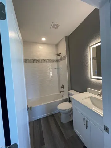 Bathroom featuring a textured wall, dark wood-type flooring, vanity, and shower / tub combination