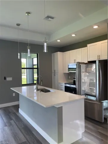 Kitchen featuring fridge, dark wood finished floors, white cabinetry, an island with sink, and range