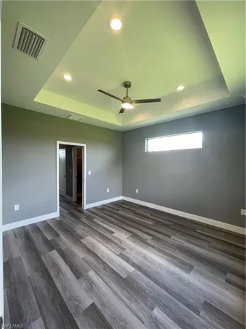 Unfurnished room with a tray ceiling, recessed lighting, ceiling fan, and dark wood finished floors