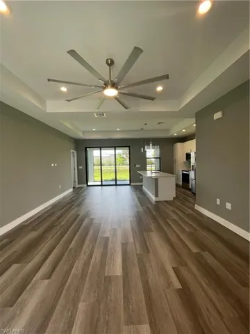 Unfurnished living room featuring a raised ceiling, a ceiling fan, dark wood finished floors, and recessed lighting