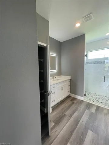 Full bath featuring vanity, dark wood-type flooring, a stall shower, a textured wall, and recessed lighting