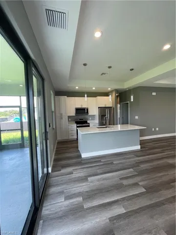 Kitchen featuring a tray ceiling, white cabinets, pendant lighting, stainless steel appliances, and an island with sink