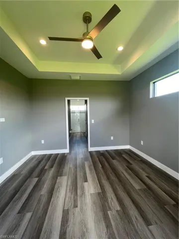 Unfurnished room with a raised ceiling, a ceiling fan, dark wood-type flooring, and recessed lighting