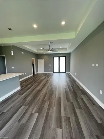 Unfurnished living room featuring a raised ceiling, dark wood-style floors, a ceiling fan, and recessed lighting