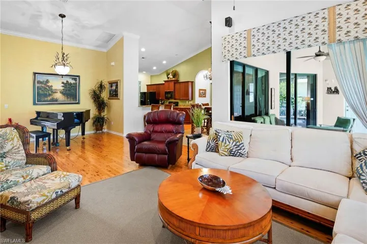 Living room featuring ornamental crown molding, bamboo flooring, chandeliers and double fan paddle ceiling fan, patio door to lanai with custom valance and drape, wood plantation shutters, wonderful natural lighing.