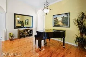 Living area with arched walkways, decorative columns, wood finished floors, baseboards, and a chandelier