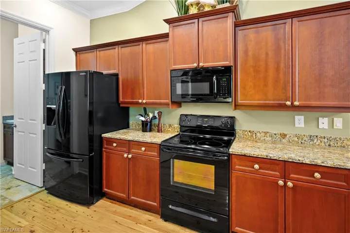 Kitchen featuring black appliances, ornamental molding, light wood finished floors, and light stone countertops