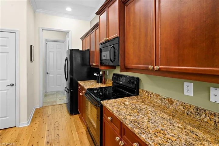Kitchen with black appliances, light stone countertops, light wood-style floors, crown molding, and baseboards