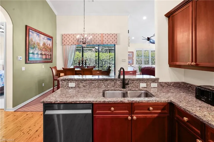 Kitchen with a sink, light wood-style flooring, light stone counters, a peninsula, and decorative light fixtures