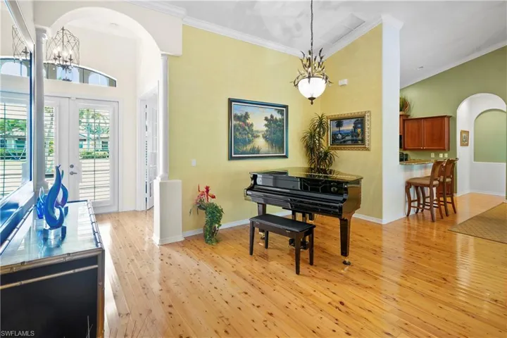 Living area featuring arched walkways, a chandelier, light wood-style flooring, ornamental molding, and french doors