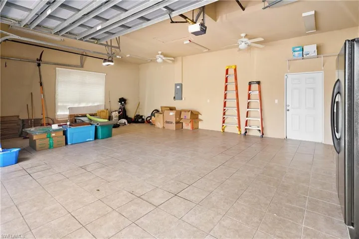 Garage featuring freestanding refrigerator, a garage door opener, electric panel, and a ceiling fan