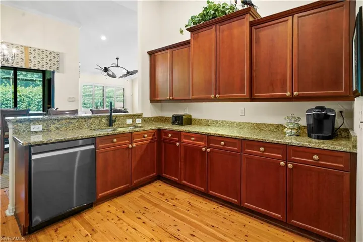 Kitchen featuring stainless steel dishwasher, a sink, light wood-style flooring, a peninsula, and light stone counters