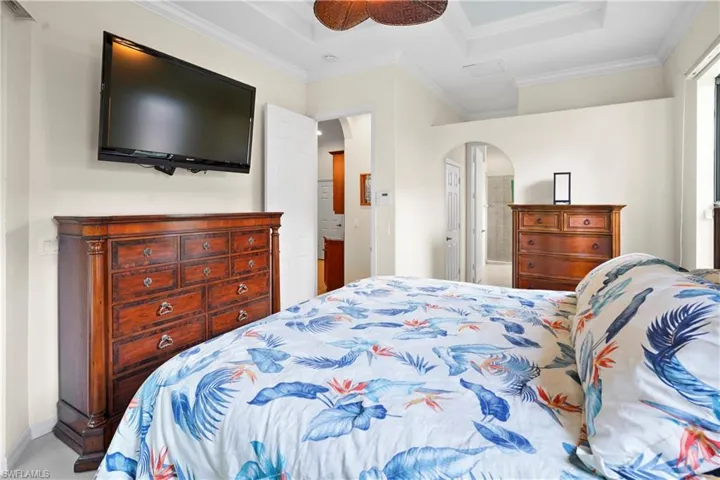 Bedroom with arched walkways, crown molding, a ceiling fan, and a tray ceiling