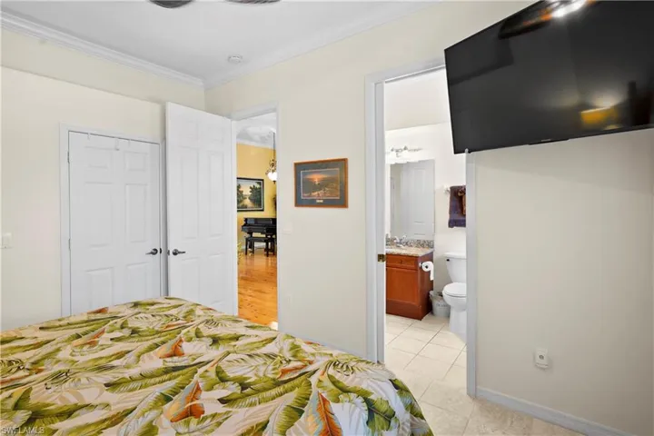 Bedroom with crown molding, light tile patterned flooring, a closet, connected bathroom, and baseboards