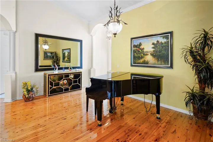 Living area featuring ornate columns, arched walkways, ornamental molding, wood finished floors, and baseboards