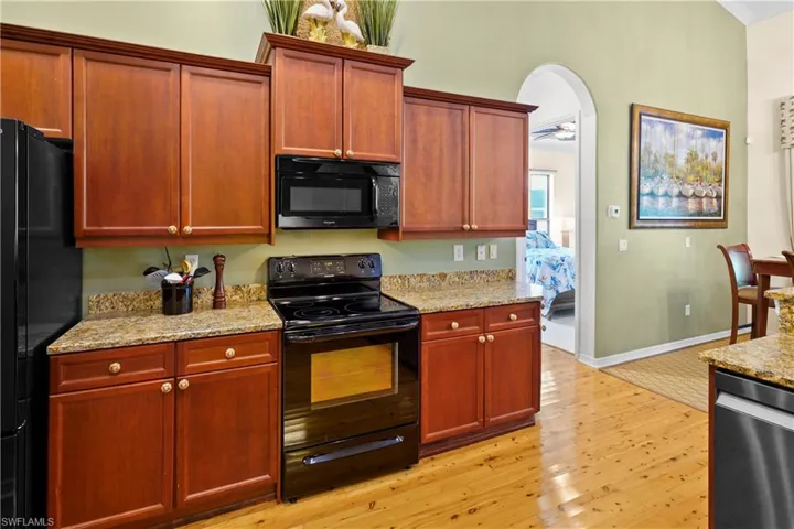 Kitchen with black appliances, light wood finished floors, light stone counters, arched walkways, and baseboards