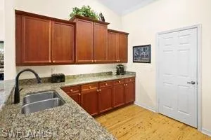 Kitchen with a sink, vaulted ceiling, light wood-style floors, light stone countertops, and baseboards