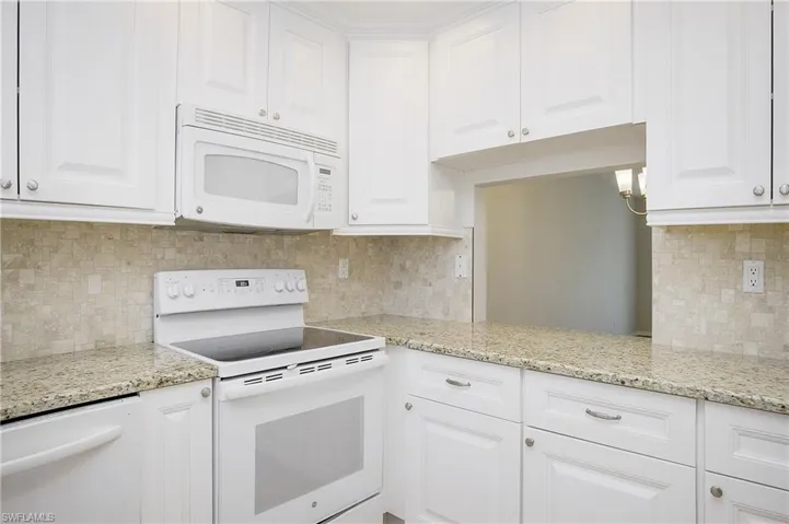 Kitchen featuring light stone counters, white cabinetry, white appliances, and tasteful backsplash