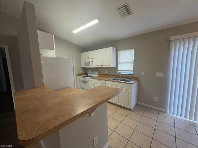 Kitchen with white appliances, white cabinets, a peninsula, a breakfast bar, and lofted ceiling