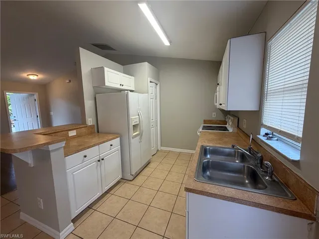 Kitchen with white cabinets, white appliances, a kitchen breakfast bar, light tile patterned floors, and a peninsula