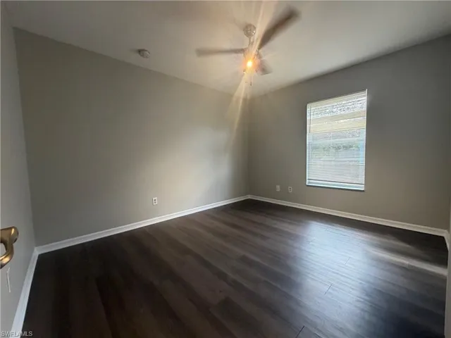 Spare room with dark wood-type flooring and baseboards
