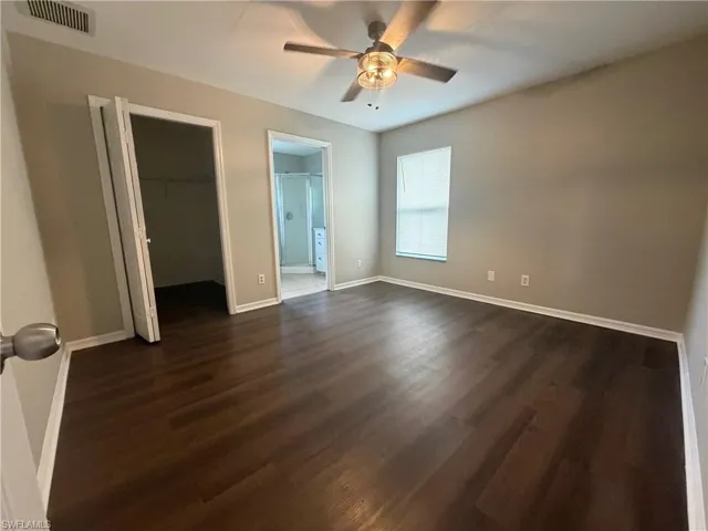 Unfurnished bedroom with a walk in closet, a ceiling fan, dark wood-type flooring, and connected bathroom
