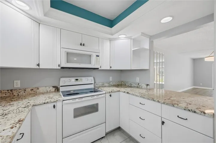 Kitchen featuring white appliances, white cabinetry, open shelves, light stone countertops, and recessed lighting