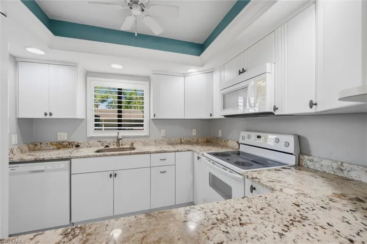 Kitchen with white appliances, white cabinetry, light stone countertops, ceiling fan, and recessed lighting