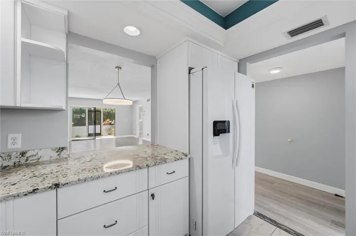 Kitchen with white fridge with ice dispenser, white cabinetry, light stone countertops, pendant lighting, and recessed lighting