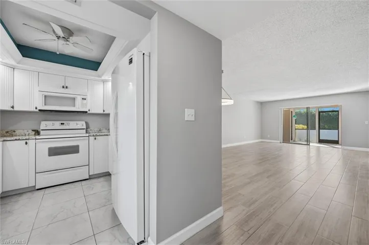 Kitchen featuring white appliances, white cabinetry, ceiling fan, light stone countertops, and a textured ceiling