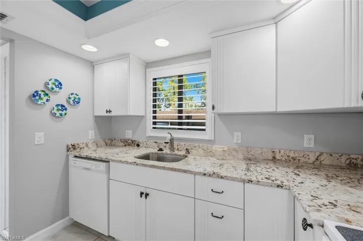 Kitchen with white cabinetry, dishwasher, recessed lighting, and light stone counters
