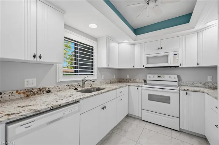 Kitchen featuring white appliances, white cabinets, a raised ceiling, and recessed lighting