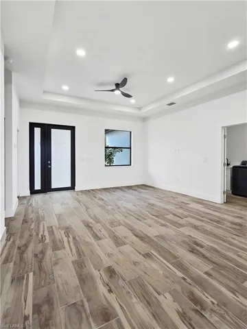 Unfurnished living room featuring light wood-type flooring, ceiling fan, recessed lighting, and a raised ceiling