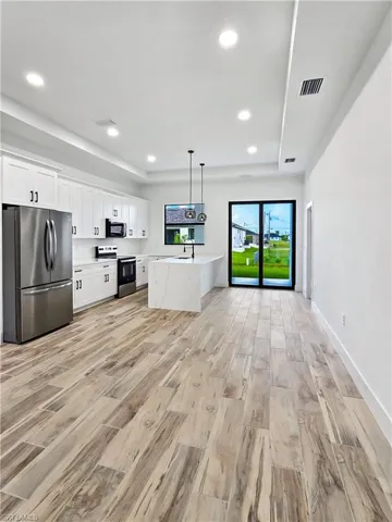 Kitchen with stainless steel appliances, light wood-style flooring, white cabinetry, decorative light fixtures, and a raised ceiling